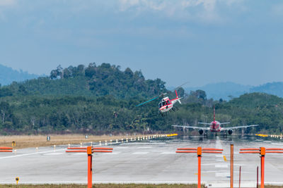 Airplane and helicopter at airport runway against sky on sunny day