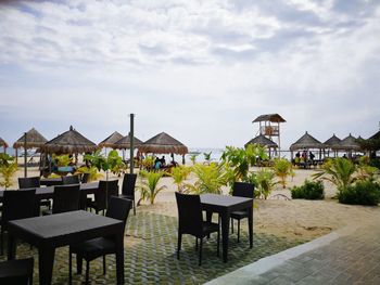 Empty chairs and table at beach against sky