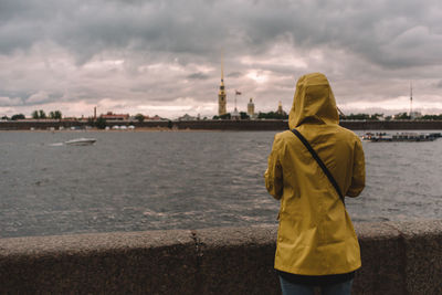 Girl in yellow raincoat. traveler admires of a neva river and peter and paul fortress in petersburg.