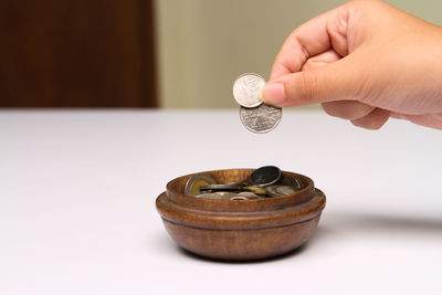 Cropped hand putting coins in container on table