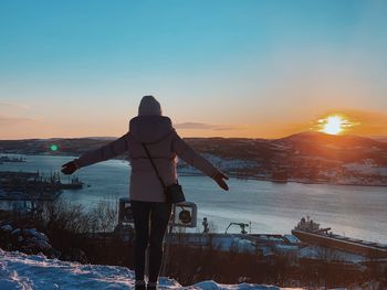 Rear view of person standing in snow against sky during sunset