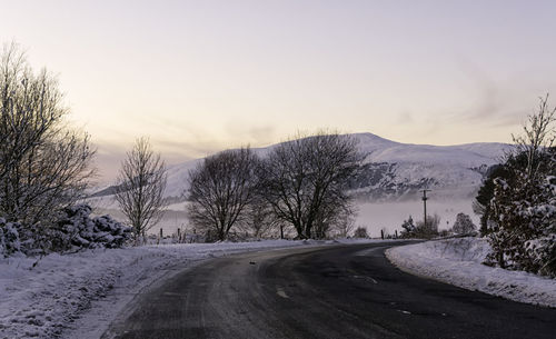 Road amidst bare trees during winter against sky