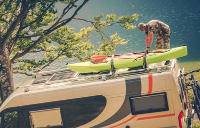 Mid adult man holding kayak on car roof against lake