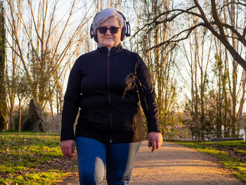 Portrait of senior woman walking while listening to music on footpath in park