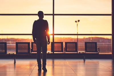 Rear view of man at airport against sky during sunset
