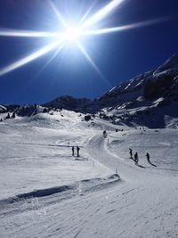 People skiing on snowcapped mountain against bright sun