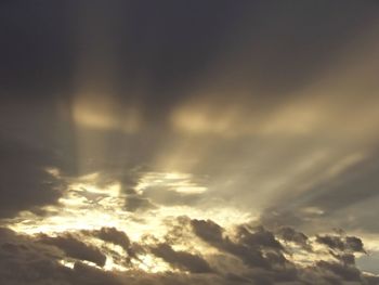 Low angle view of sunlight streaming through clouds