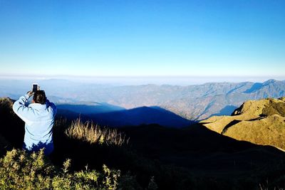 Rear view of people standing on mountain against blue sky