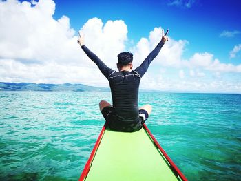 Rear view of man gesturing peace sign while sitting on boat in sea against sky