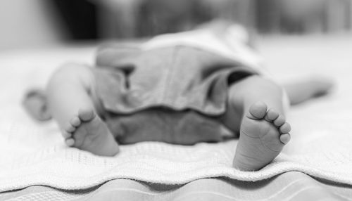 Low section of baby boy lying on bed at home