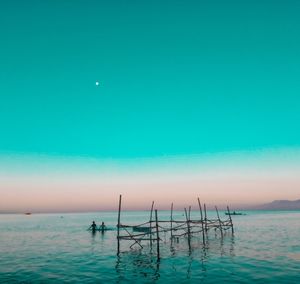 People in sea against clear sky during sunset