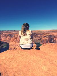 Rear view of woman sitting on rock in desert