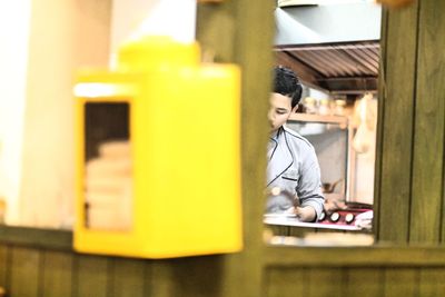 Young male chef working in kitchen seen through window