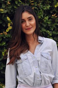 Portrait of smiling young woman standing against plants at park