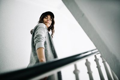 Portrait of a smiling young woman standing on staircase against wall