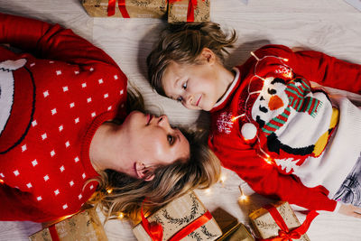 Mom and daughter in christmas sweaters sit and lie among a large number of gift boxes