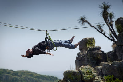 Low angle view of man jumping on rock against sky