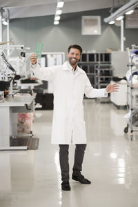 Full length portrait of happy engineer showing machine part in manufacturing industry