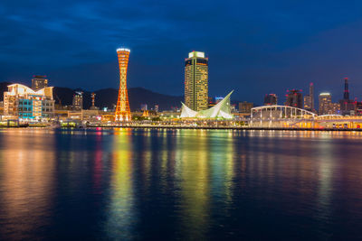 Illuminated city by river against sky at night