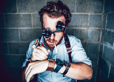 Portrait of young man holding sunglasses against wall