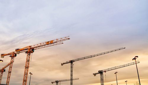 Low angle view of cranes at construction site against sky