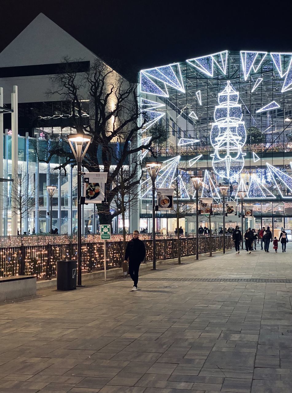 PEOPLE WALKING ON STREET AGAINST ILLUMINATED BUILDINGS IN CITY