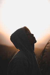 Close-up of young man wearing hoodie against sky during sunset
