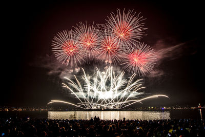 High angle view of crowd by river against firework display at night