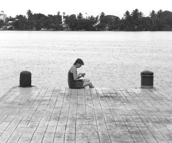 Side view of young woman sitting on lake against trees