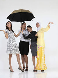 Portrait of smiling female friends sharing umbrella against white background