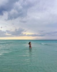 Rear view of woman in sea against sky during sunset