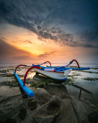 Boat moored on beach against sky during sunset