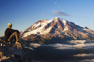 Side view of man sitting on mountain against clear sky