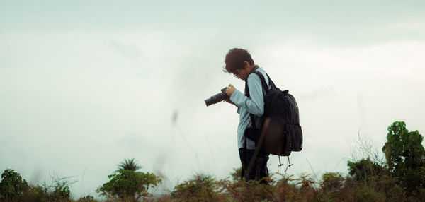 Man holding camera standing against sky