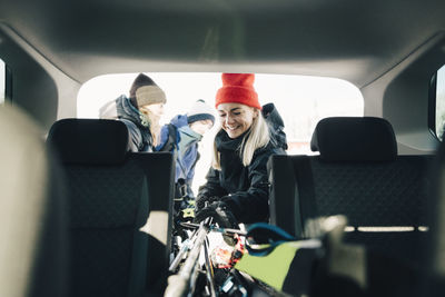 Smiling woman loading skis in car trunk with friends