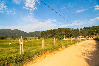 Road passing through field against cloudy sky