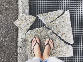 Low section of woman standing on broken stone tile over metal grate