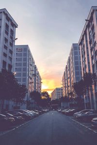 Road amidst buildings against sky during sunset in city