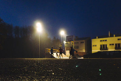 Men on illuminated street against clear sky at night