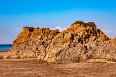 Rock formations on beach against blue sky