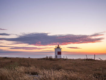 Lighthouse on beach against sky during sunset