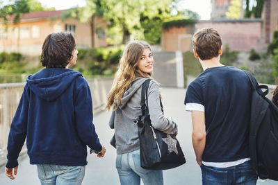 Rear view portrait of smiling female teenager walking with male friends on bridge