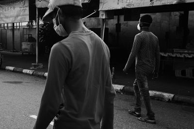 Rear view of man wearing face mask walking on street in city 