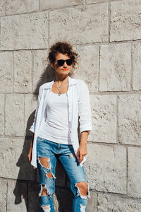 Young woman wearing sunglasses standing against wall
