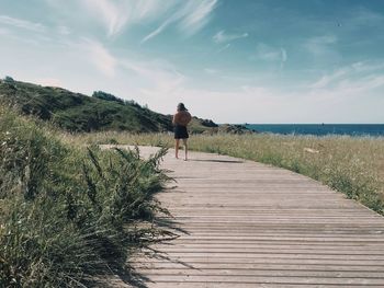 Woman walking on boardwalk at beach against sky