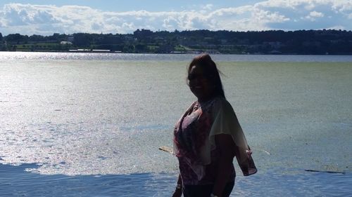 Rear view of woman standing at beach against sky