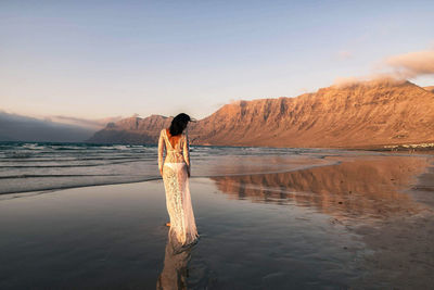 Rear view of woman standing on beach against sky