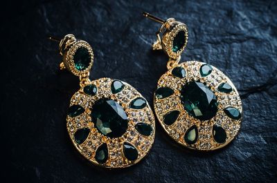 Gold earrings with green stones on a black background