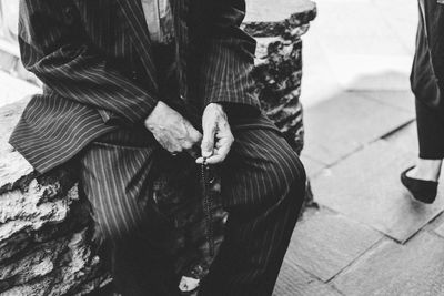 Midsection of man holding prayer beads while sitting outdoors