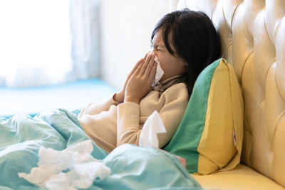 Side view of girl sneezing while lying on bed at home